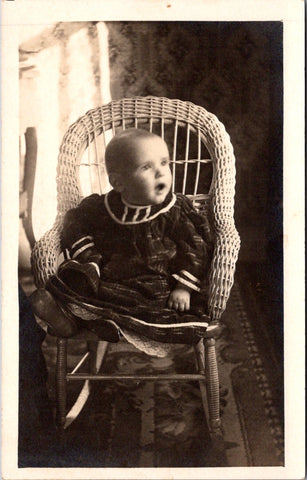 People - Child - seated in a wicker rocking chair in flannel dress RPPC - 800883