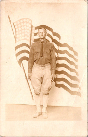 Military Man in uniform - posing in front of a flowing US flag - RPPC - E23237