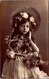 People - Girl - large hat, basket of flowers, hand to face - @1911 RPPC - NL0894