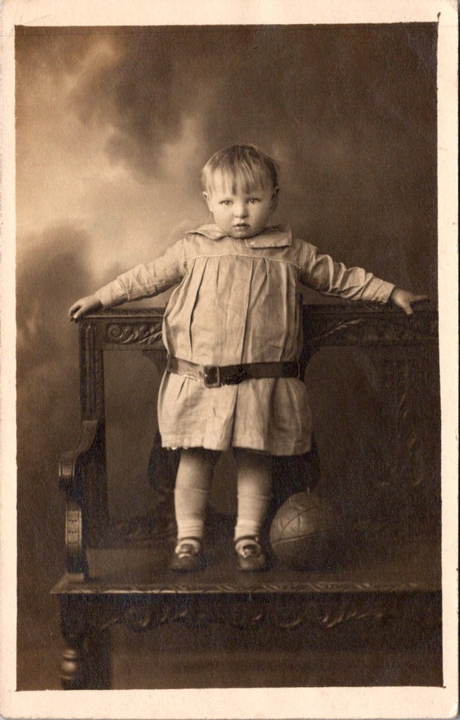 People - Child - standing on carved bench near leather ball - studio RPPC - SH7260